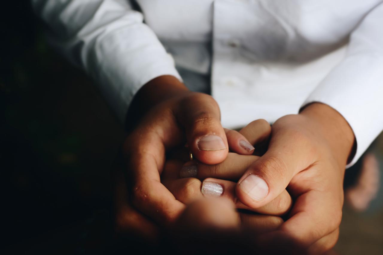 Image of persons holding hands, main person shown wearing a white button down shirt. 