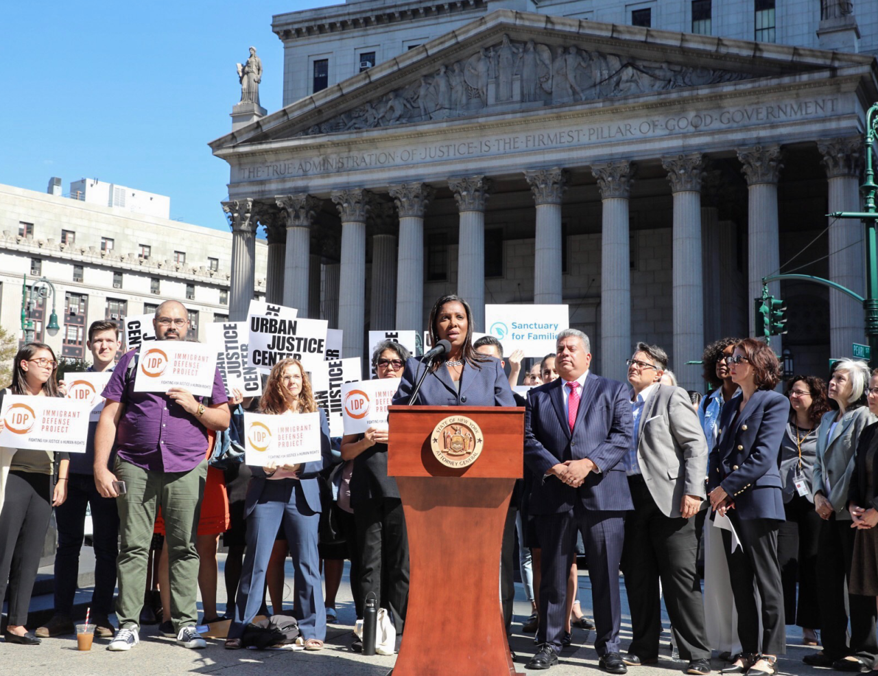 AG James standing at a podium with a group of people behind her outside a courthouse